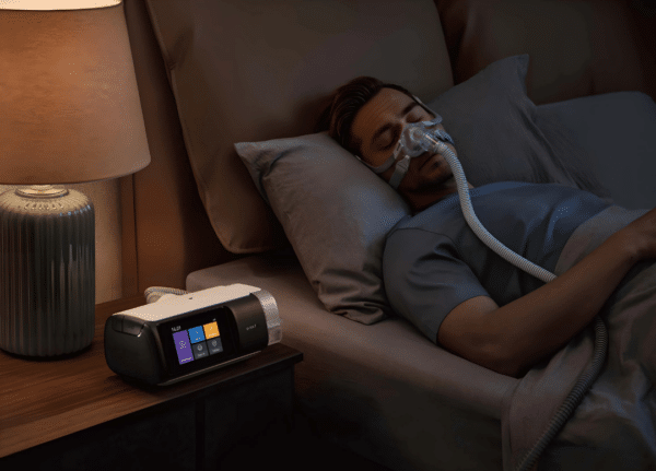 Hombre durmiendo pacíficamente en la cama. El dispositivo de terapia de sueño CPAP Yuwell Breathcare III YH-680 está visible y encendido sobre la mesilla de noche a su lado.